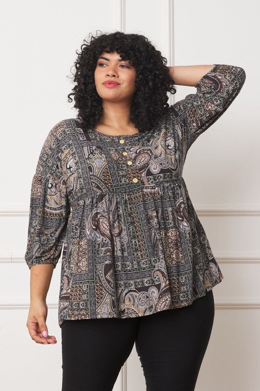 A woman with curly hair, dressed in a Plus Button Accent Paisley Top with three-quarter sleeves, and black pants, poses with one arm behind her head.