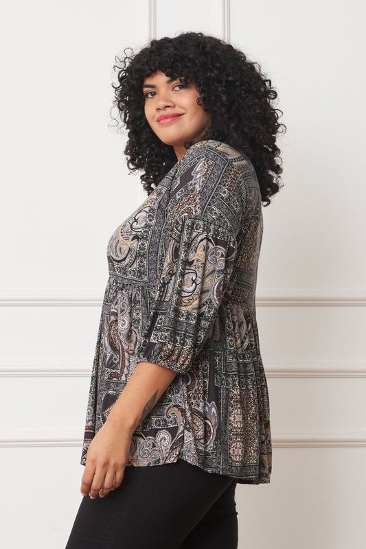 A person with curly black hair wears the Plus Button Accent Paisley Top paired with black pants, standing with one hand behind their head.