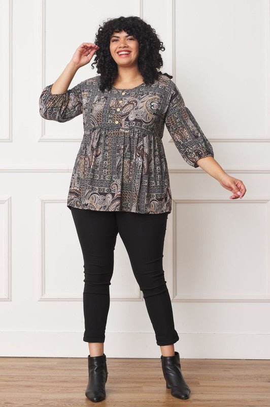 A person with curly black hair wears the Plus Button Accent Paisley Top paired with black pants, standing with one hand behind their head.