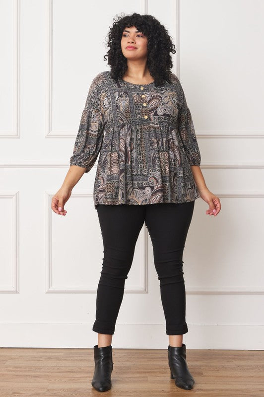 A person with curly black hair wears the Plus Button Accent Paisley Top paired with black pants, standing with one hand behind their head.