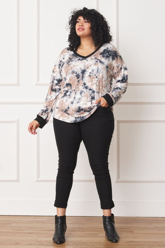 A woman with curly hair is wearing a Plus V-Neck Tie Dye Top made of 95% polyester and 5% spandex, standing in front of a white paneled wall.
