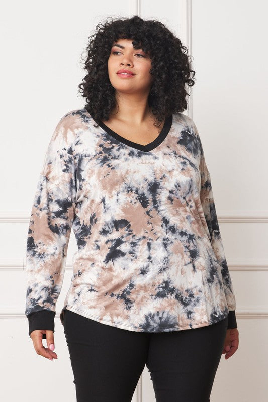 A woman with curly hair is wearing a Plus V-Neck Tie Dye Top made of 95% polyester and 5% spandex, standing in front of a white paneled wall.