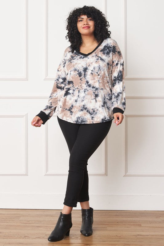 A woman with curly hair is wearing a Plus V-Neck Tie Dye Top made of 95% polyester and 5% spandex, standing in front of a white paneled wall.