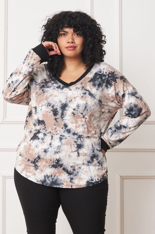 A woman with curly hair is wearing a Plus V-Neck Tie Dye Top made of 95% polyester and 5% spandex, standing in front of a white paneled wall.