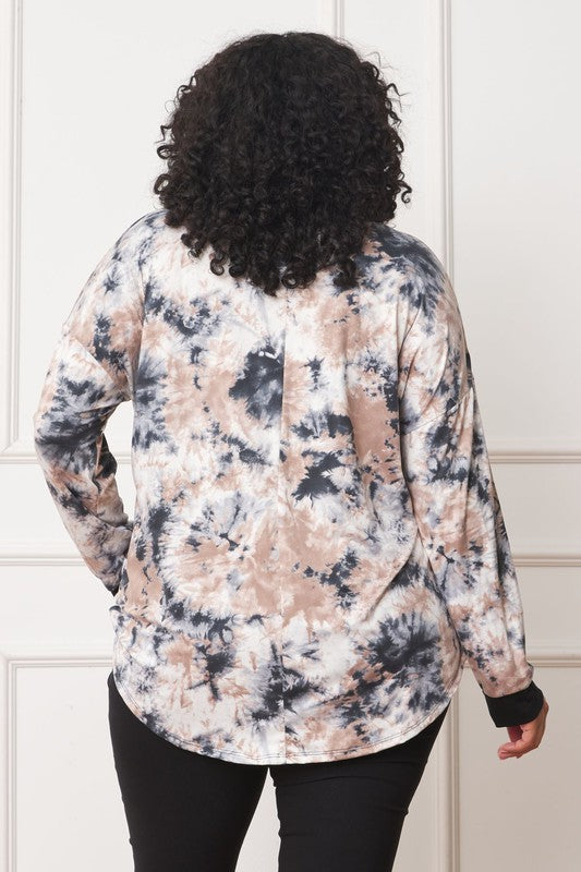 A woman with curly hair is wearing a Plus V-Neck Tie Dye Top made of 95% polyester and 5% spandex, standing in front of a white paneled wall.