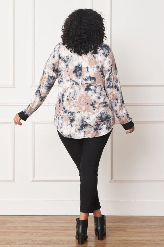 A woman with curly hair is wearing a Plus V-Neck Tie Dye Top made of 95% polyester and 5% spandex, standing in front of a white paneled wall.