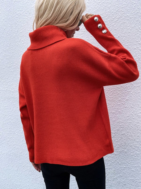 A woman modeling the Women's Long Sleeve Mock Neck Sweater in dark green, featuring button details on the sleeves, paired with black pants and posing against a textured white wall.