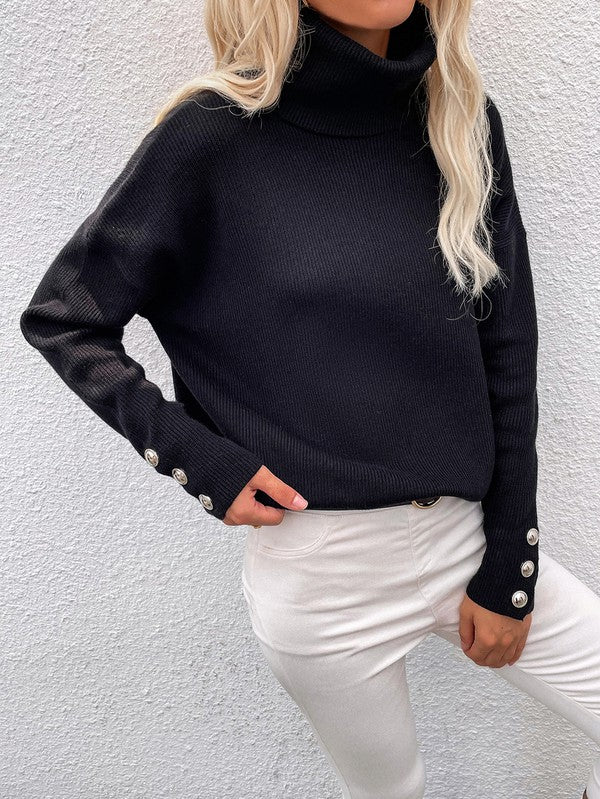 A woman modeling the Women's Long Sleeve Mock Neck Sweater in dark green, featuring button details on the sleeves, paired with black pants and posing against a textured white wall.