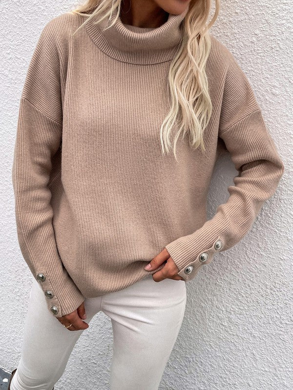 A woman modeling the Women's Long Sleeve Mock Neck Sweater in dark green, featuring button details on the sleeves, paired with black pants and posing against a textured white wall.