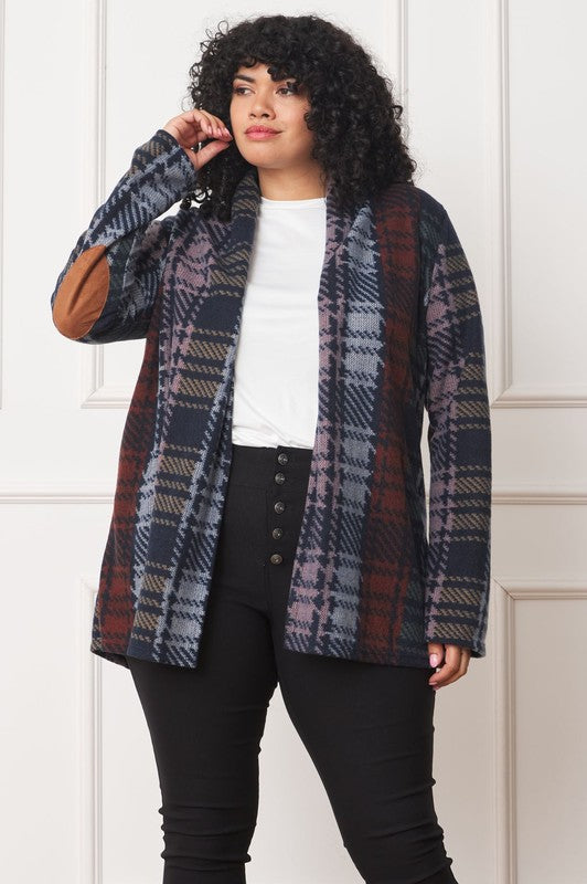 A woman wearing the Multi Color Plaid Elbow Patch Cardigan, made in the United States, strikes a pose with one hand on her cardigan and the other near her head, styled with a black top and black pants.