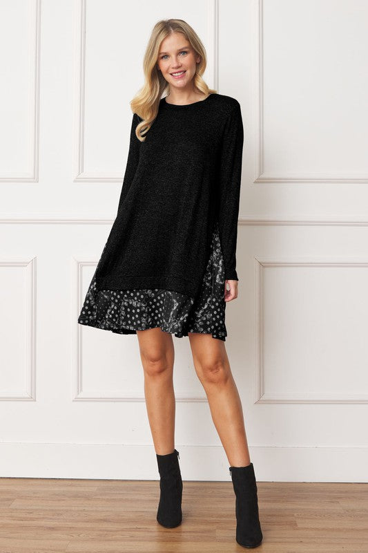 A woman with long blonde hair wears a grey long-sleeve sweater layered over the Mock Layered Bandana Paisley Mini Dress. She is standing indoors against a plain white wall and looking downward.