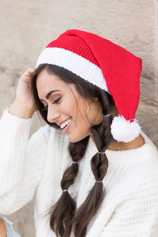 A smiling woman wearing a long Santa Stocking Beanie Hat with a knit pom accent.