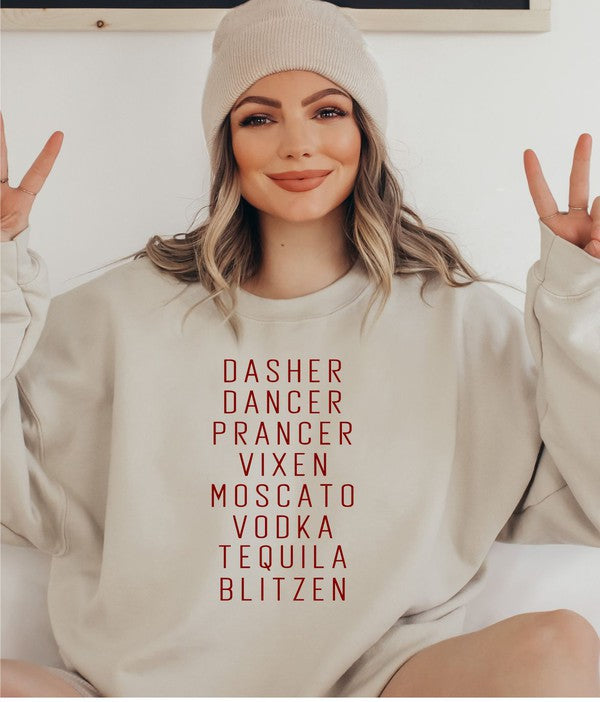 A person stands in front of a weathered wooden door, wearing the Dasher Dancer Prancer Vixen Boutique Sweatshirt, which is a light gray crew neck with maroon print listing reindeer and alcoholic beverages. They are also dressed in light-colored pants and large black sunglasses.