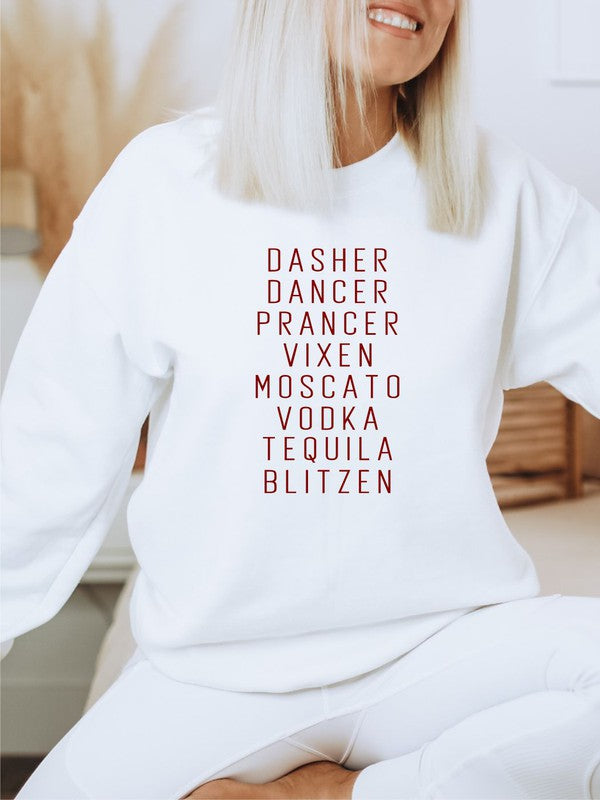 A person stands in front of a weathered wooden door, wearing the Dasher Dancer Prancer Vixen Boutique Sweatshirt, which is a light gray crew neck with maroon print listing reindeer and alcoholic beverages. They are also dressed in light-colored pants and large black sunglasses.