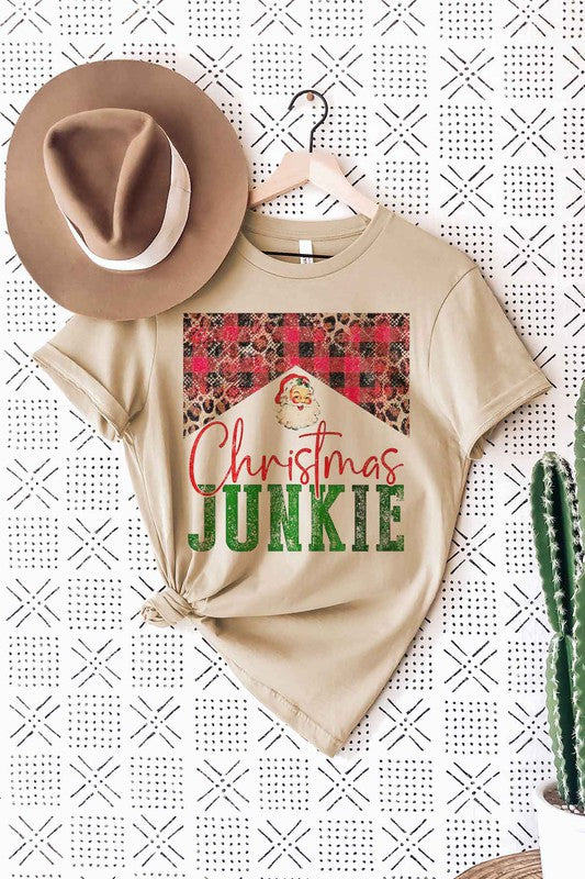 A woman wearing a light pink "CHRISTMAS JUNKIE GRAPHIC PLUS SIZE TEE / T-SHIRT" made from premium cotton, with a holiday design and a brown hat, standing against a plain background.