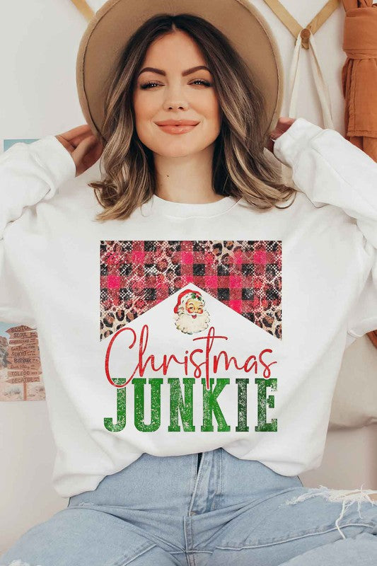 A person is seen wearing denim shorts paired with a CHRISTMAS JUNKIE GRAPHIC SWEATSHIRT, which boasts festive graphics such as a Santa face, leopard print, and a plaid pattern. Crafted from premium cotton and designed with unisex sizing to ensure the perfect fit.