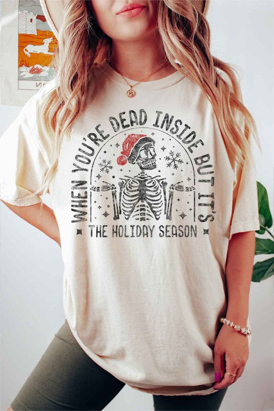 A young woman with long hair in a pink hat is wearing the CHRISTMAS SKELETON GRAPHIC TEE / T-SHIRT, crafted from premium cotton, featuring a white base with the text "When you're dead inside but it's the holiday season.