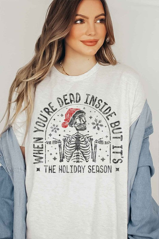 A young woman with long hair in a pink hat is wearing the CHRISTMAS SKELETON GRAPHIC TEE / T-SHIRT, crafted from premium cotton, featuring a white base with the text "When you're dead inside but it's the holiday season.