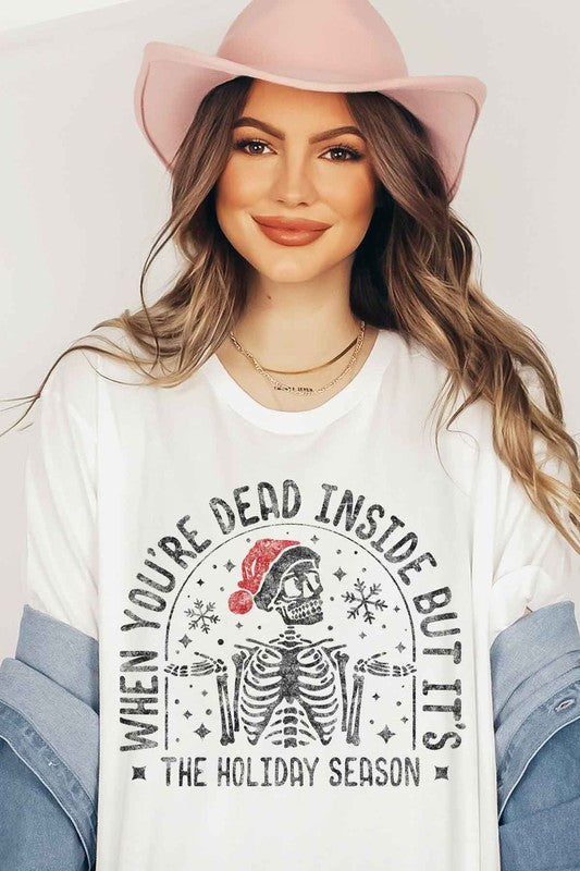 A person wearing a tan hat and a pink CHRISTMAS SKELETON GRAPHIC PLUS SIZE TEE / T-SHIRT featuring a skeleton in a Santa hat, with the text "When you're dead inside but it's the holiday season." This unisex sizing tee captures the perfect mix of humor and festive spirit.