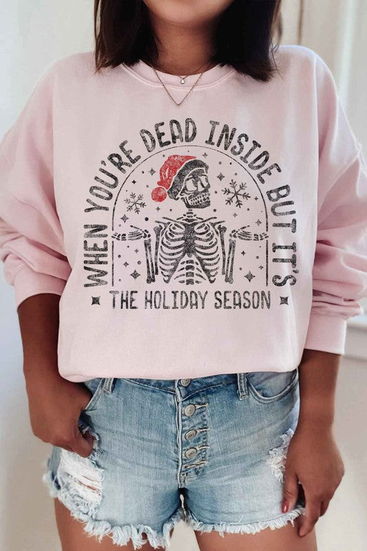 Person wearing the Christmas Skeleton Graphic Sweatshirt in premium cotton gray, which features a festive skeleton with a Santa hat and the text "When you’re dead inside, but it’s the holiday season." A perfect addition to your holiday wardrobe.