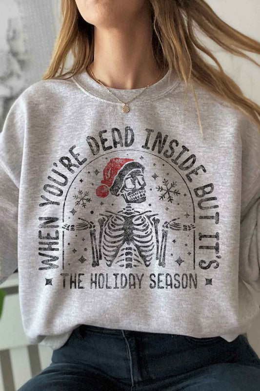 Person wearing the Christmas Skeleton Graphic Sweatshirt in premium cotton gray, which features a festive skeleton with a Santa hat and the text "When you’re dead inside, but it’s the holiday season." A perfect addition to your holiday wardrobe.