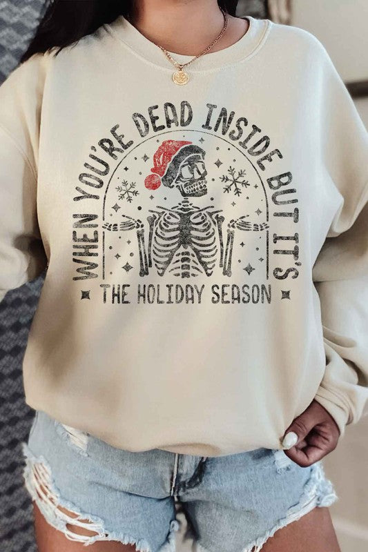 Person wearing the Christmas Skeleton Graphic Sweatshirt in premium cotton gray, which features a festive skeleton with a Santa hat and the text "When you’re dead inside, but it’s the holiday season." A perfect addition to your holiday wardrobe.