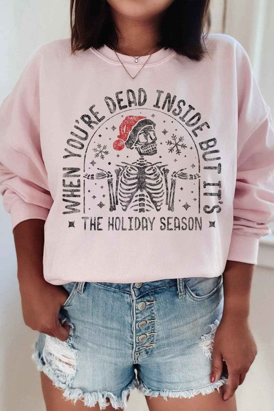 A person wearing the CHRISTMAS SKELETON GRAPHIC PLUS SIZE SWEATSHIRT, featuring a skeleton in a Santa hat and the text "When you're dead inside but it's the holiday season.