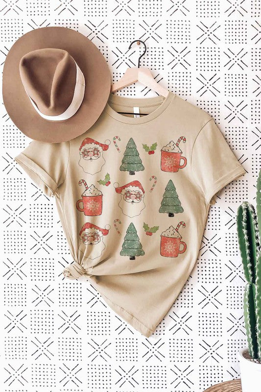 A woman wearing a pink hat and a white CHRISTMAS COLLECTION GRAPHIC TEE / T-SHIRT with festive holiday prints of Santa Claus, Christmas trees, candy canes, and mugs of hot chocolate stands against a light background. This classic fit is part of our exclusive Christmas collection.