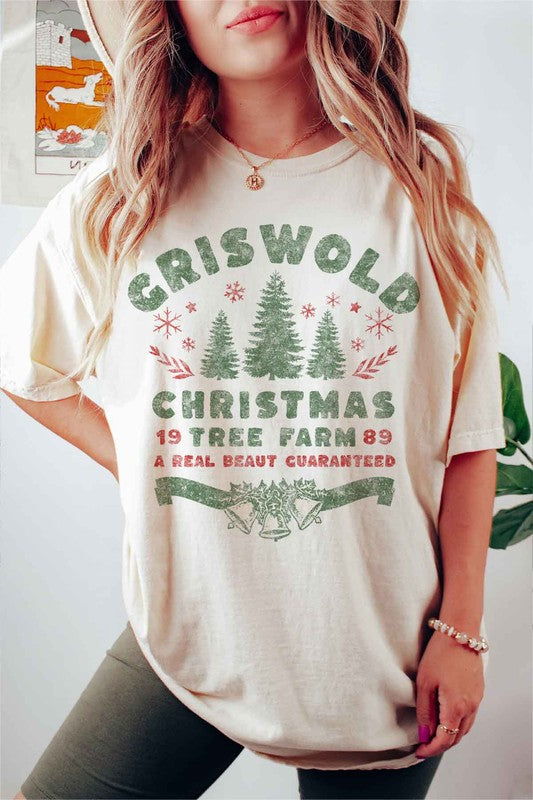 A woman wearing a pink hat and a CHRISTMAS TREE FARM GRAPHIC TEE that reads, "Criswold Christmas Tree Farm '89 - A Real Beaut Guaranteed," featuring Christmas trees and festive designs.