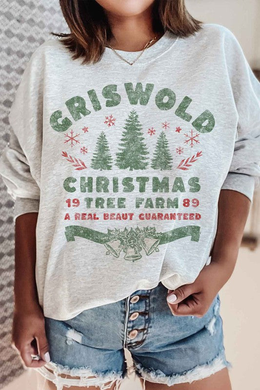 Person wearing a cozy CHRISTMAS TREE FARM GRAPHIC PLUS SIZE SWEATSHIRT in white, adorned with green and red text: "Griswold Christmas Tree Farm '89, A Real Beaut Guaranteed," showcasing festive Christmas trees and holiday decorations. Perfect for a charming visit to the Christmas tree farm!