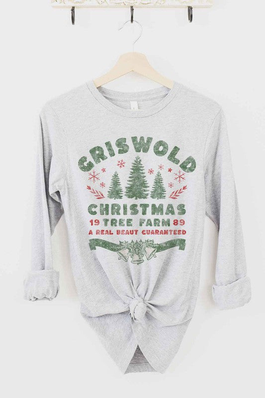 A premium cotton CHRISTMAS TREE FARM LONG SLEEVE TEE in cream hangs on a wooden hanger. It features green and red text and graphics promoting "Griswold Christmas Tree Farm" with a festive design of trees and snowflakes.