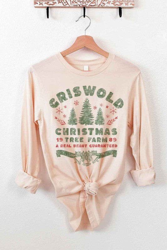 A premium cotton CHRISTMAS TREE FARM LONG SLEEVE TEE in cream hangs on a wooden hanger. It features green and red text and graphics promoting "Griswold Christmas Tree Farm" with a festive design of trees and snowflakes.