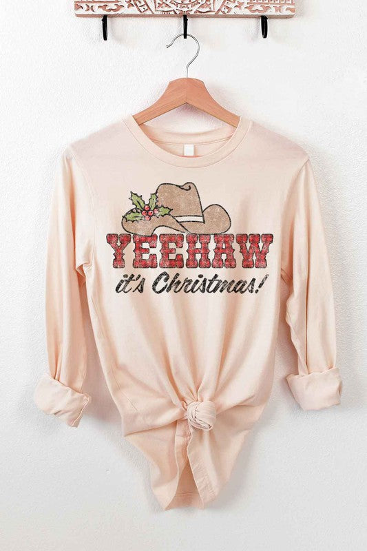 The YEEHAW COUNTRY CHRISTMAS LONG SLEEVE TEE, crafted from premium cotton, is a cream long-sleeved shirt with a tied hem on a hanger. It features a cowboy hat, holly, and the text "YEEHAW COUNTRY CHRISTMAS!