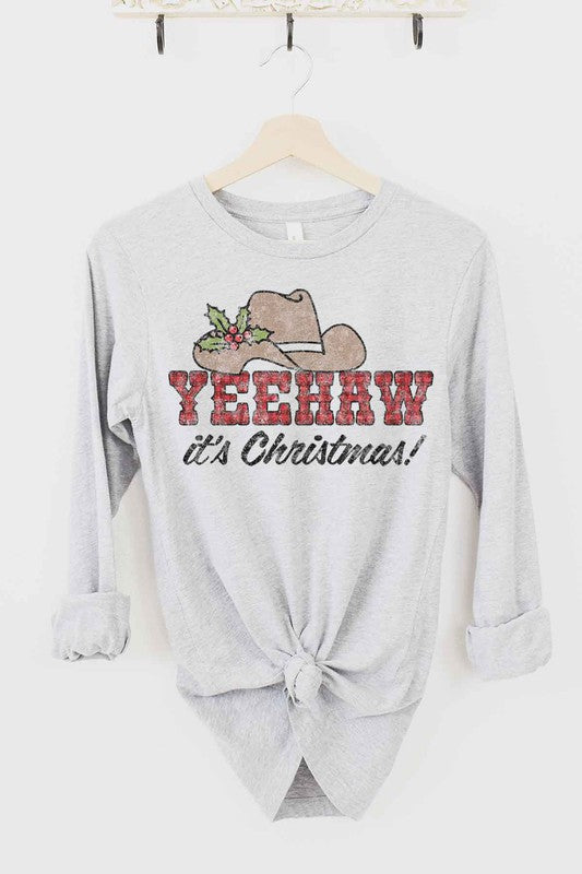 The YEEHAW COUNTRY CHRISTMAS LONG SLEEVE TEE, crafted from premium cotton, is a cream long-sleeved shirt with a tied hem on a hanger. It features a cowboy hat, holly, and the text "YEEHAW COUNTRY CHRISTMAS!