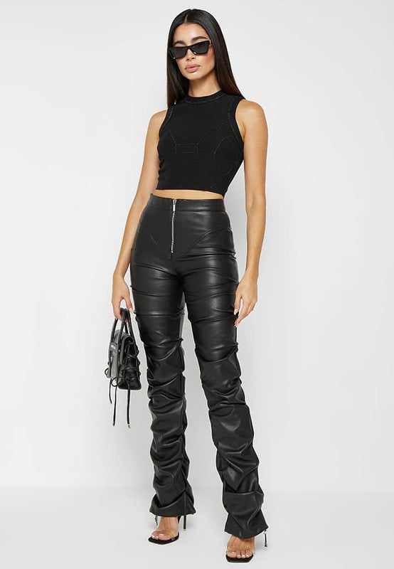 A woman stands against a plain background, wearing a black sleeveless top paired with the SEXY PU LEATHER PANTS that have a high waist and skinny style. She accessorizes with high heels, sunglasses, and holds a small black handbag in her left hand.