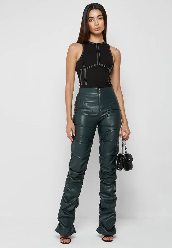 A woman stands against a plain background, wearing a black sleeveless top and high-waisted SEXY PU LEATHER PANTS in dark green. The pants are made from polyester fabric. She holds a small black handbag and has long, straight hair.