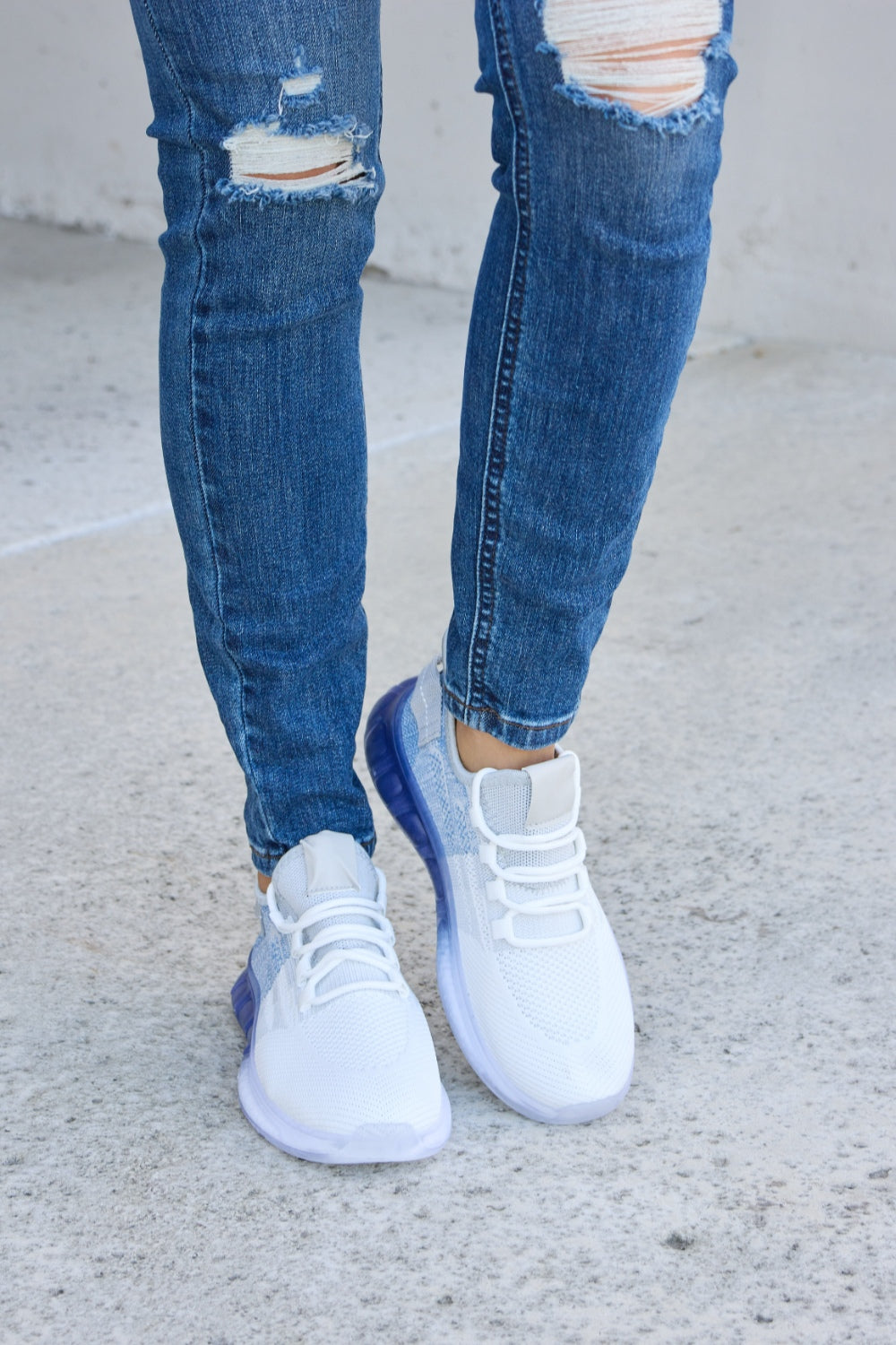 A person wearing distressed blue jeans and a pair of Forever Link Gradient Lace-Up Mesh Breathable Athletic Shoes, standing on a concrete surface.