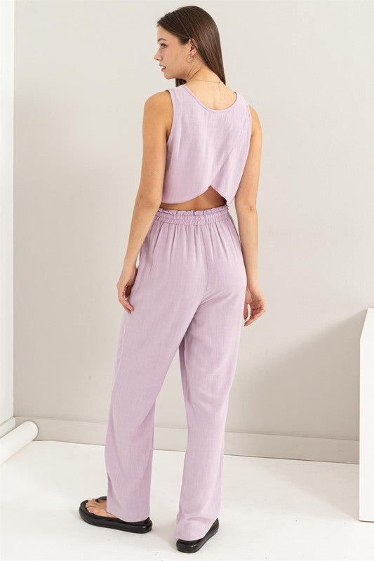 A person is seated on the floor, dressed in a soft lavender D-Linen Blended Top and Pants Set, complemented by chic black sandals.