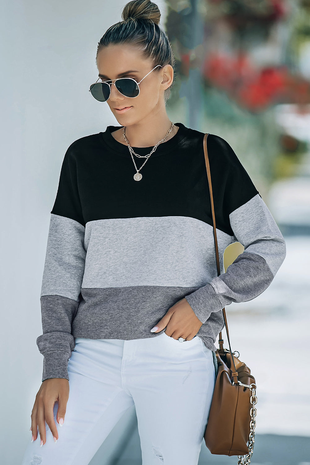 A person wearing a Colorblock Black Contrast Stitching Sweatshirt with Slits featuring black, gray, and light gray stripes, paired with white pants that resemble leggings and carrying a brown bag, shown from behind.