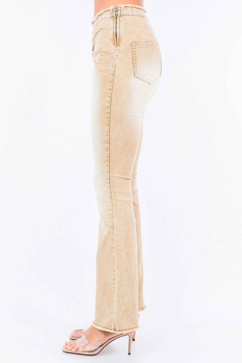 A person is wearing American Bazi V-Cut Ruched Flare Pants in light beige with frayed hems, paired with transparent high-heeled sandals.