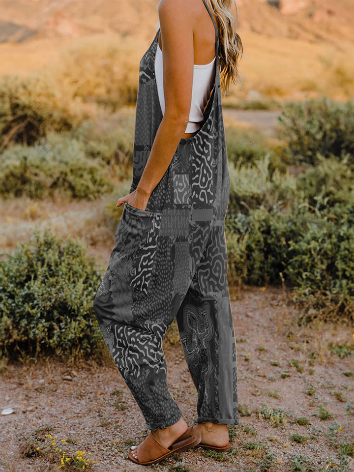 A person standing outdoors in front of rocky terrain, wearing a Full Size Printed V-Neck Sleeveless Jumpsuit and a hat.