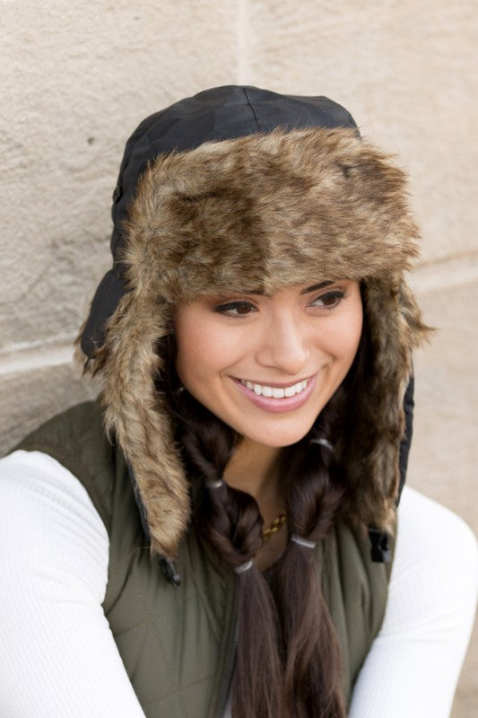 A woman smiling while adjusting a whimsical animal-themed Alpine Aviator Trapper hat.