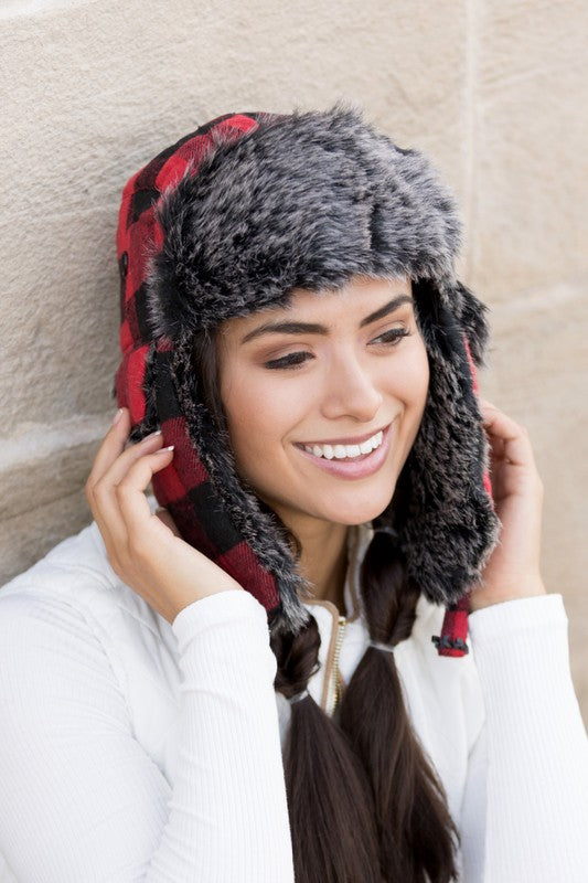 Woman smiling while wearing a checkered Buffalo Trapper Hat with ear flaps and faux fur interior.
