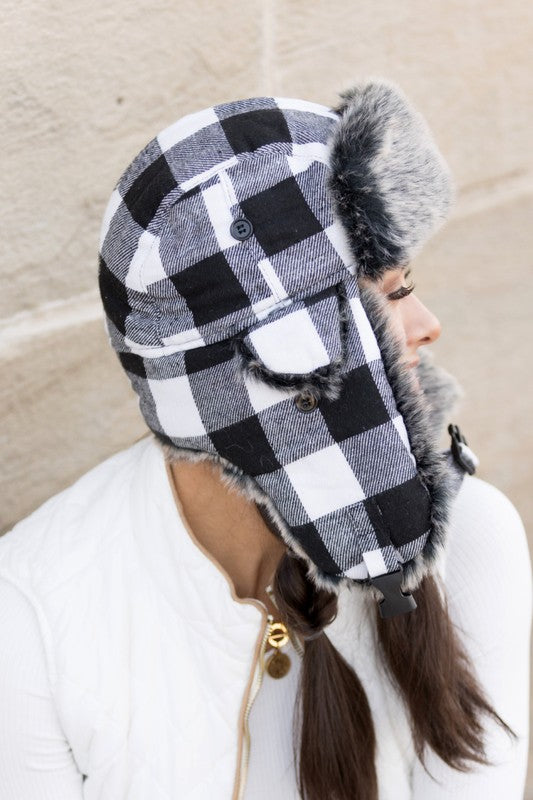 Woman smiling while wearing a checkered Buffalo Trapper Hat with ear flaps and faux fur interior.