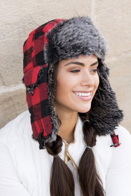 Woman smiling while wearing a checkered Buffalo Trapper Hat with ear flaps and faux fur interior.