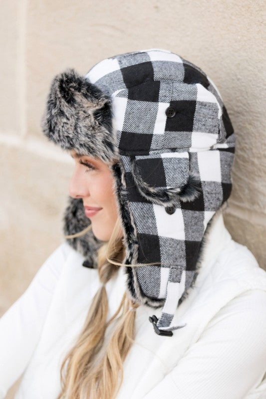 Woman smiling while wearing a checkered Buffalo Trapper Hat with ear flaps and faux fur interior.