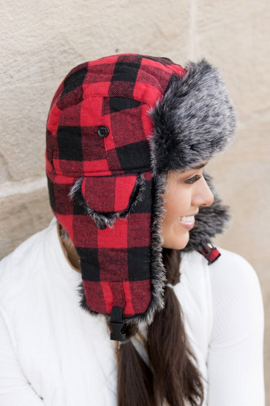 Woman smiling while wearing a checkered Buffalo Trapper Hat with ear flaps and faux fur interior.