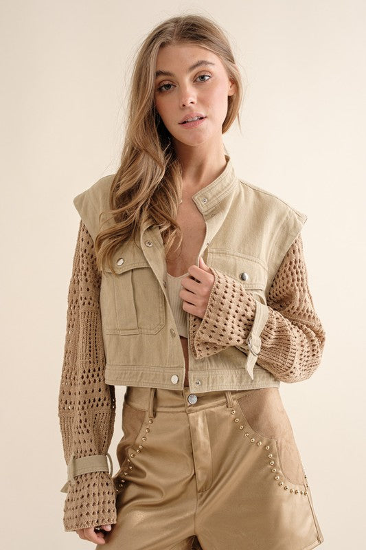 A person wearing a Twill Crop Crochet SLV Jacket and distressed denim shorts stands by a window with a red frame.