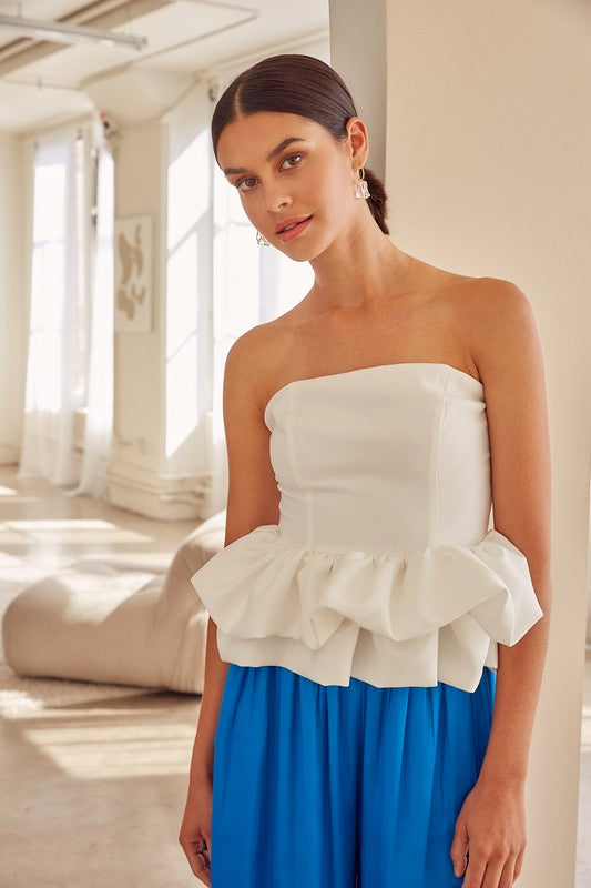 A woman stands against a neutral backdrop wearing an Off Shoulder Ruffle Top in pink, paired with a shiny black skirt, effortlessly embodying boho chic elegance.