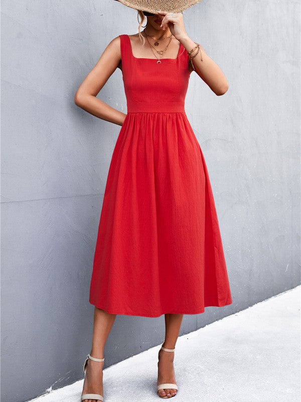 A woman in a Women's Sleeve Less Dress, featuring a vibrant red hue and crafted from 100% polyester, stands against a gray wall. She accessorizes with a wide-brimmed hat, holds a straw handbag, and complements her outfit with beige sandals.